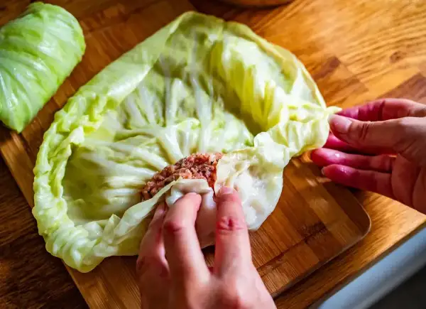 Ręce zwijają gołąbki z farszem mięsnym w liście kapusty. To początek przygotowań do pysznego dania, idealnego na przepis na gołąbki na 1kg mięsa.