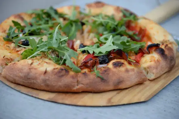Pizza z rukolą i oliwkami na drewnianej desce.