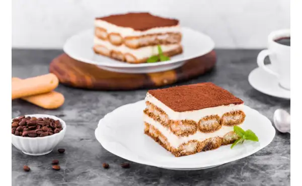 Pyszne tiramisu z warstwami kremu i biszkoptów do tiramisu, posypane kakao. Obok filiżanka kawy i ziarna kawy.