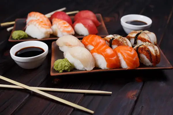 Różnorodne sushi rodzaje: nigiri z krewetką, łososiem, białym rybą i węgorzem, podane z wasabi i sosem sojowym.
